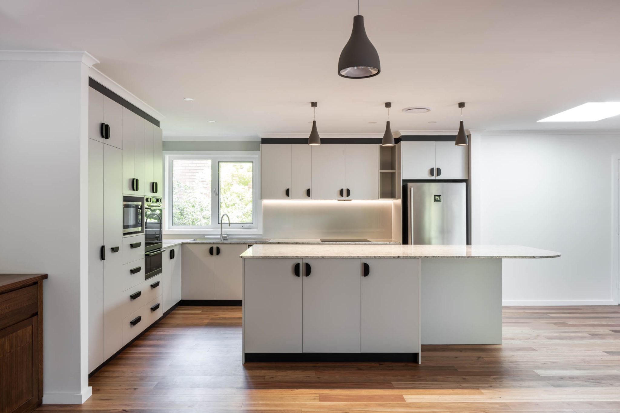 A sleek, modern kitchen with white cabinets and wood flooring, exemplifying expert residential interior design by a top interior designer in Canberra.